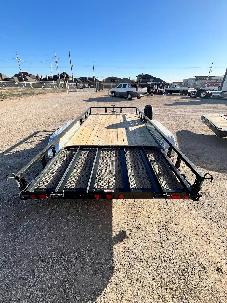 A black and gray utility trailer with a wooden bed and a ramp, parked outdoors on a sunny day.