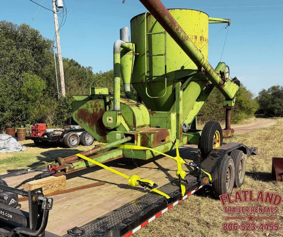Green agricultural equipment strapped to a trailer outdoors on a sunny day.