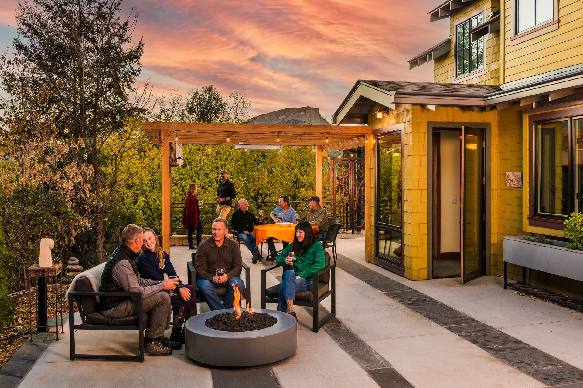 a group of people sit around a fire pit on a patio behind them the house with new windows installed by Sunglass Replacement Windows & Doors