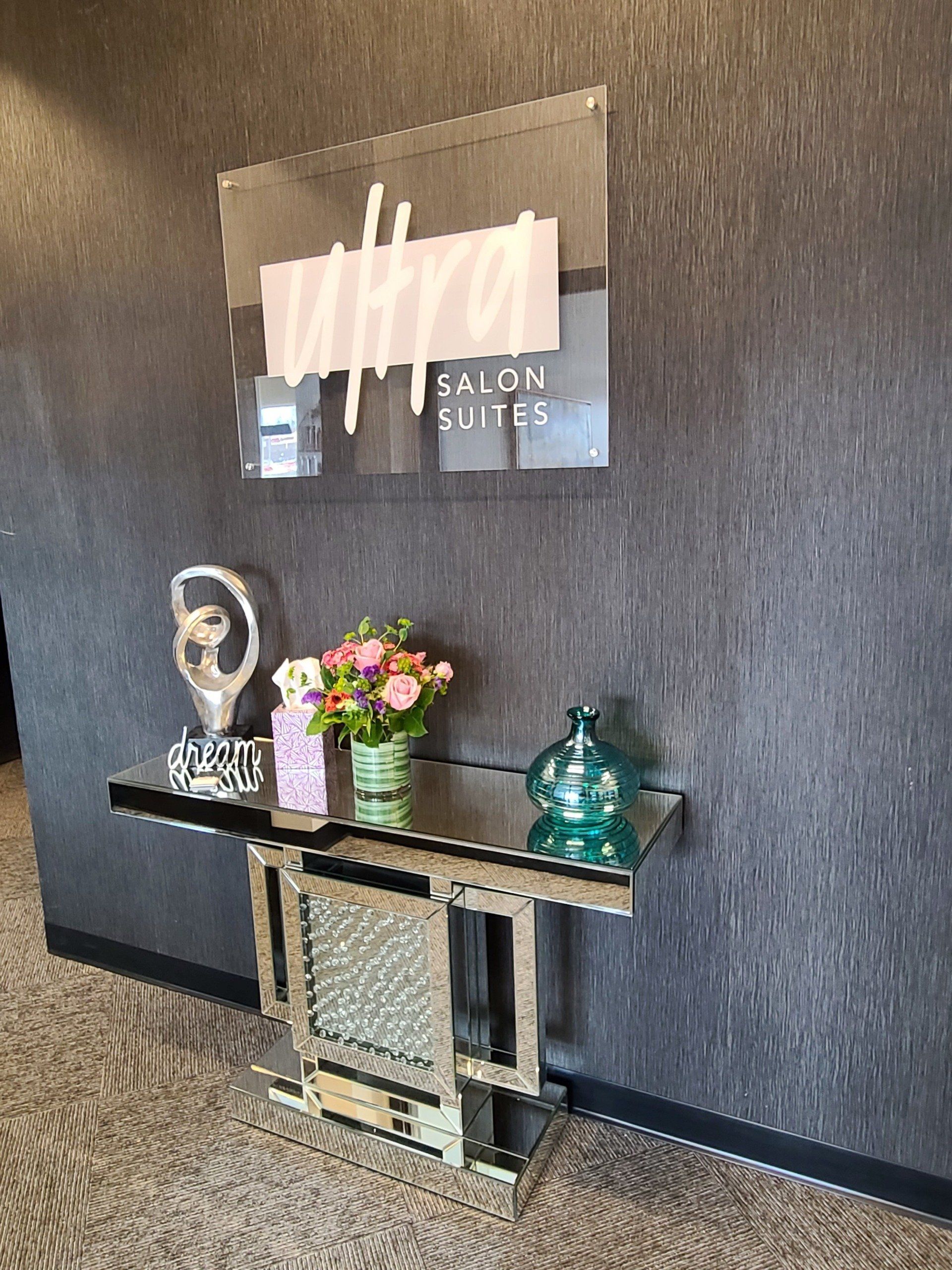 There is a sign on the wall above a table with flowers on it.