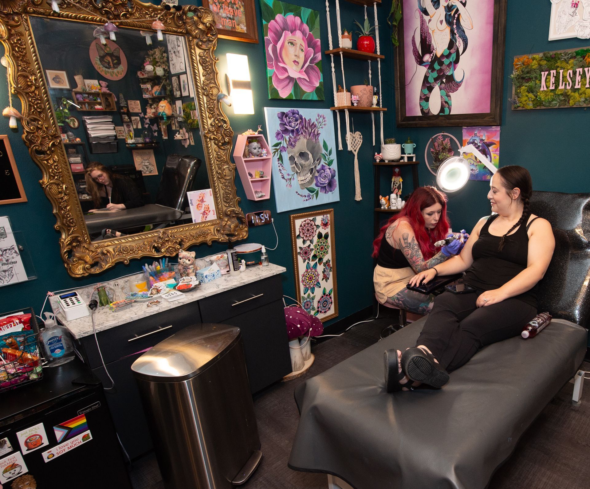 A woman is getting a tattoo on her arm while another woman looks on.