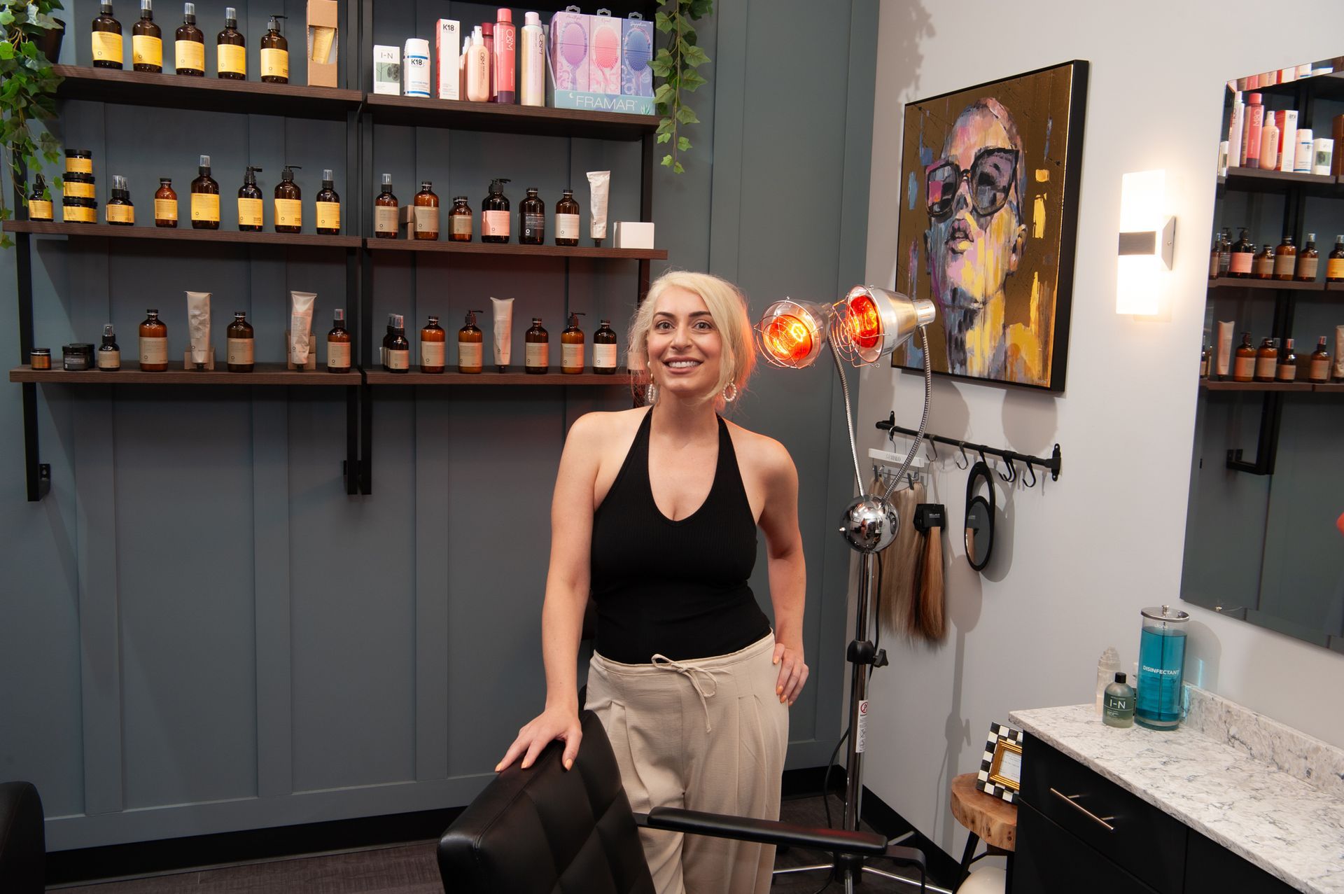 A woman is standing in a hair salon next to a chair.