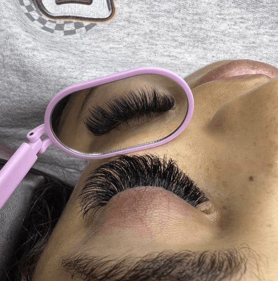 A woman is looking at her eyelashes in a mirror.