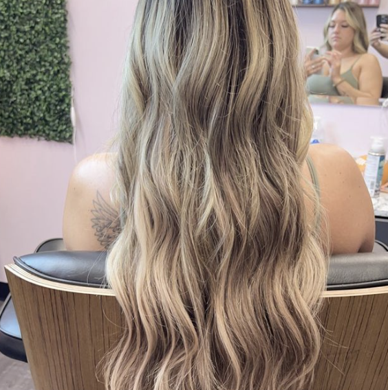 A woman with long blonde hair is sitting in a chair in front of a mirror.