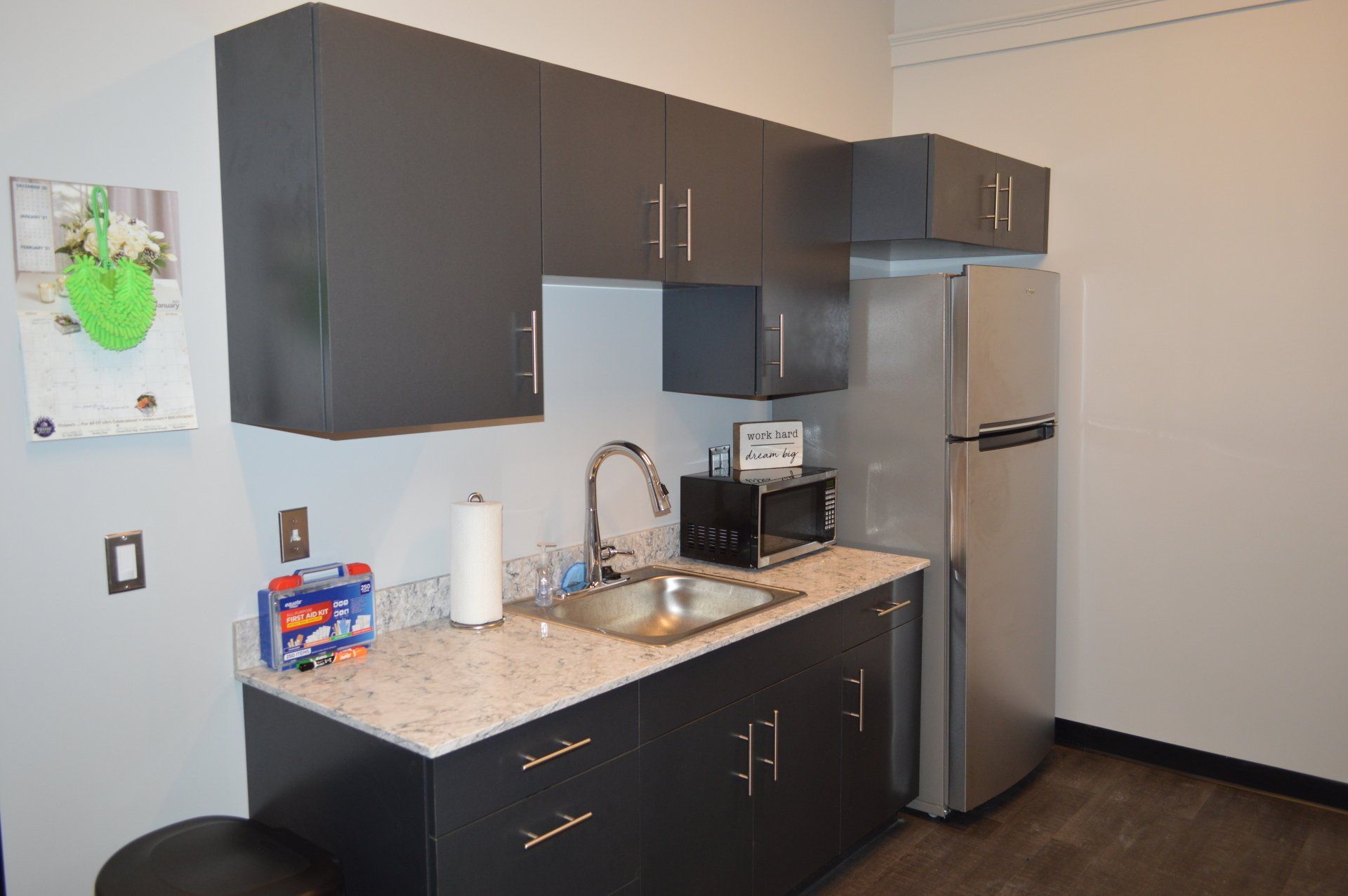 A kitchen with black cabinets , a sink , a refrigerator and a microwave.