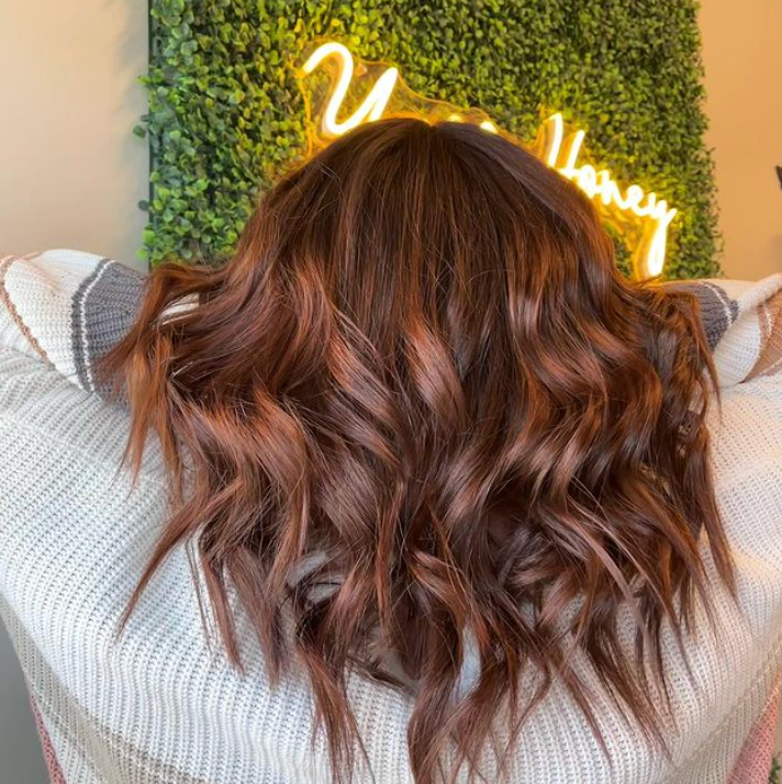 A woman with long brown hair is standing in front of a neon sign.