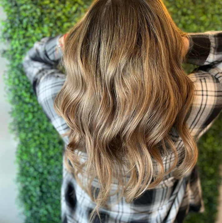 A woman with long wavy brown hair is wearing a plaid shirt.