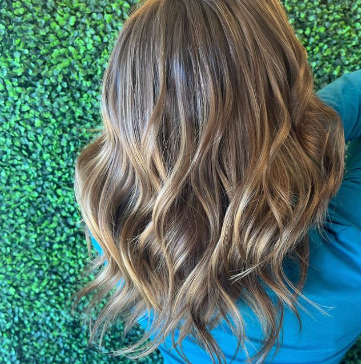 A woman with long wavy brown hair is wearing a blue shirt.