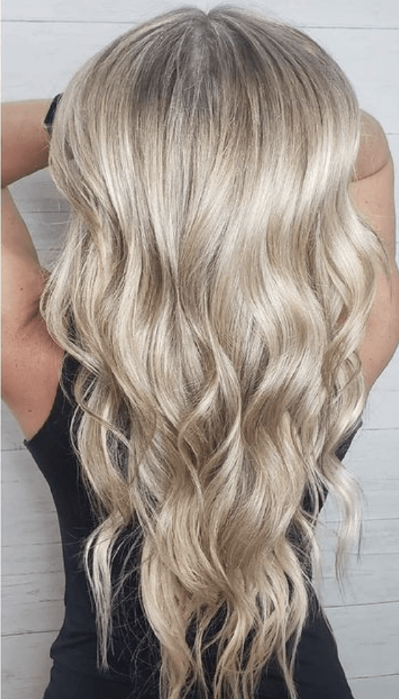 A woman with long blonde wavy hair is wearing a black tank top.