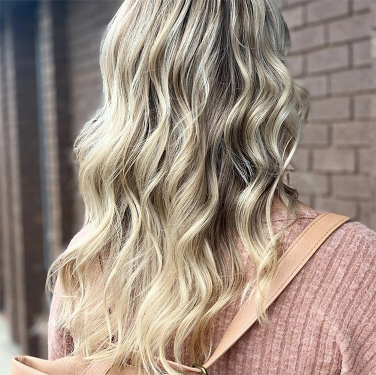 A woman with long blonde hair is wearing a pink sweater and carrying a backpack.