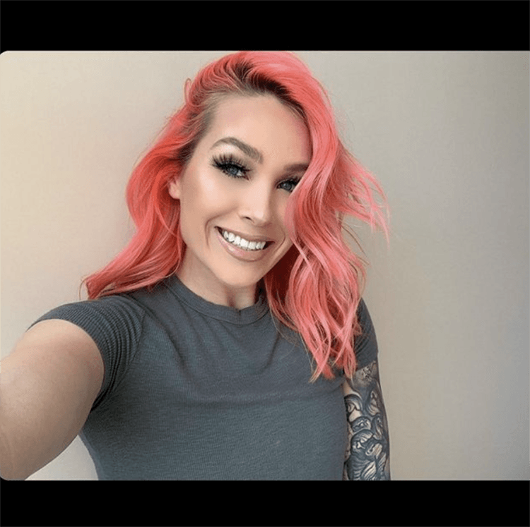 A woman with pink hair is smiling and wearing a grey shirt