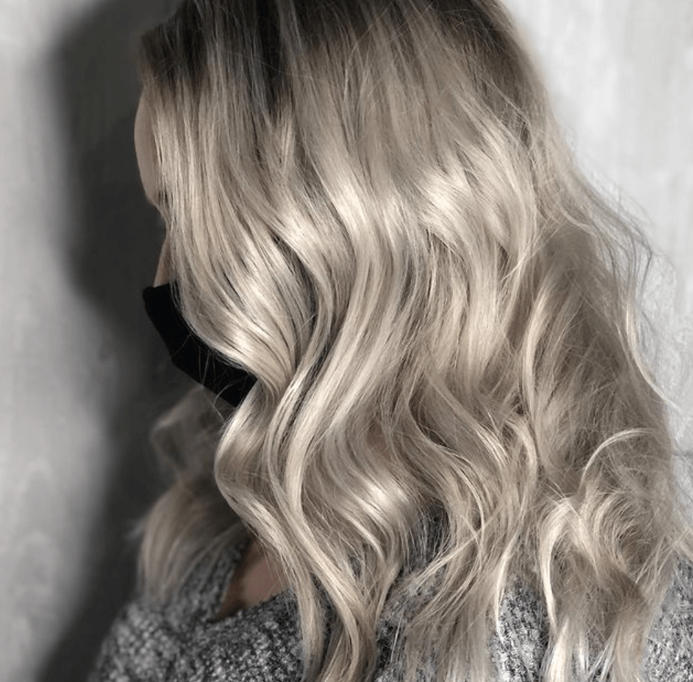 A woman with long blonde hair is wearing a sweater and a mask.