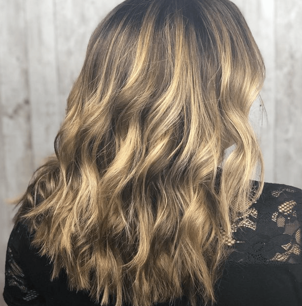 A woman with long wavy blonde hair is wearing a black lace top.