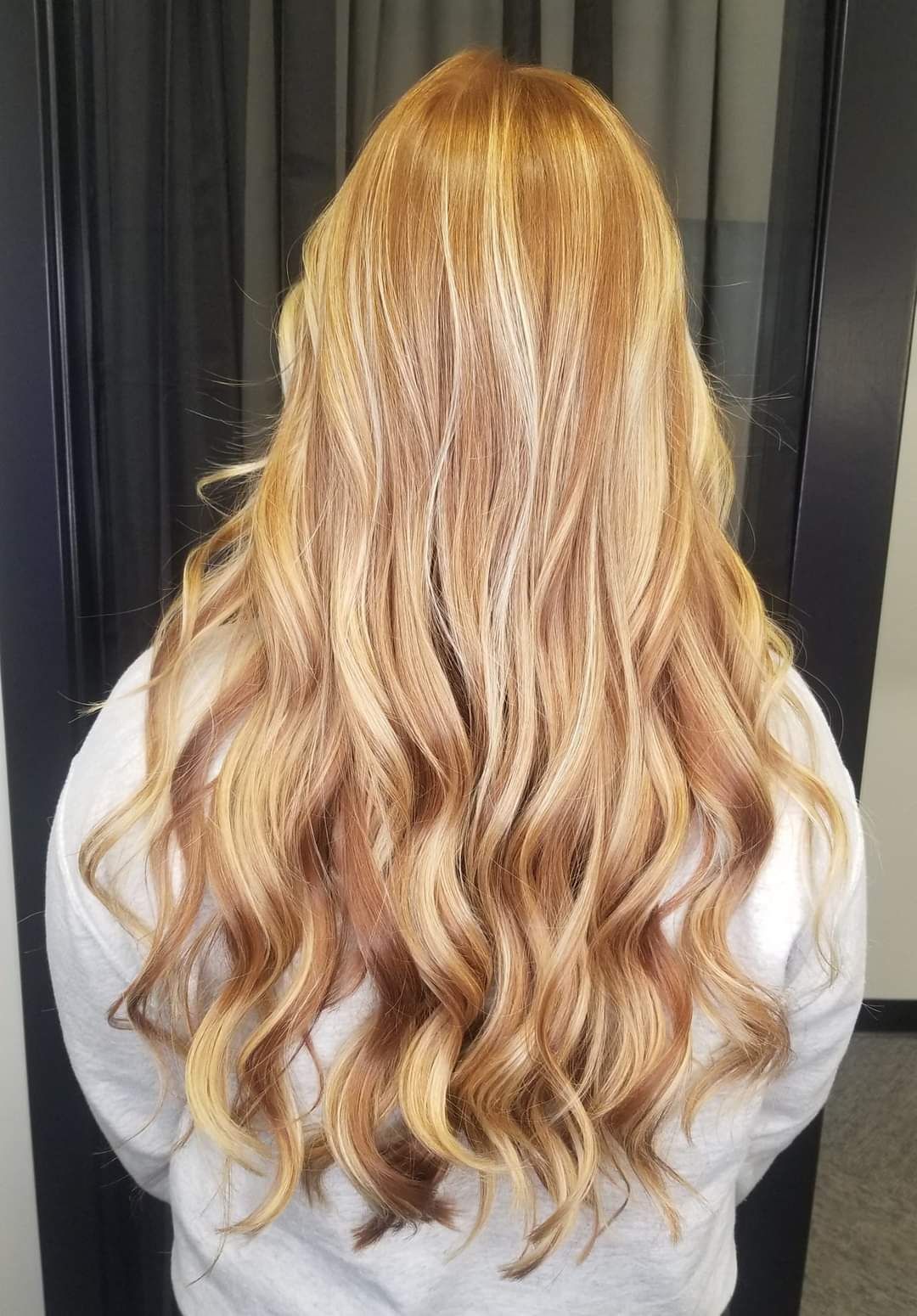 A woman with long blonde hair is wearing a white sweater and standing in front of a mirror.