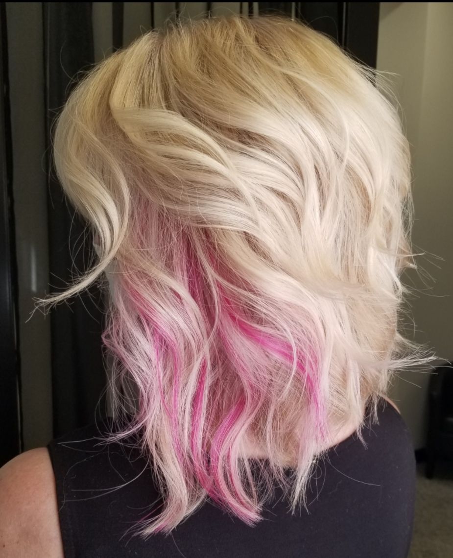 A woman with blonde hair and pink highlights is wearing a black shirt.