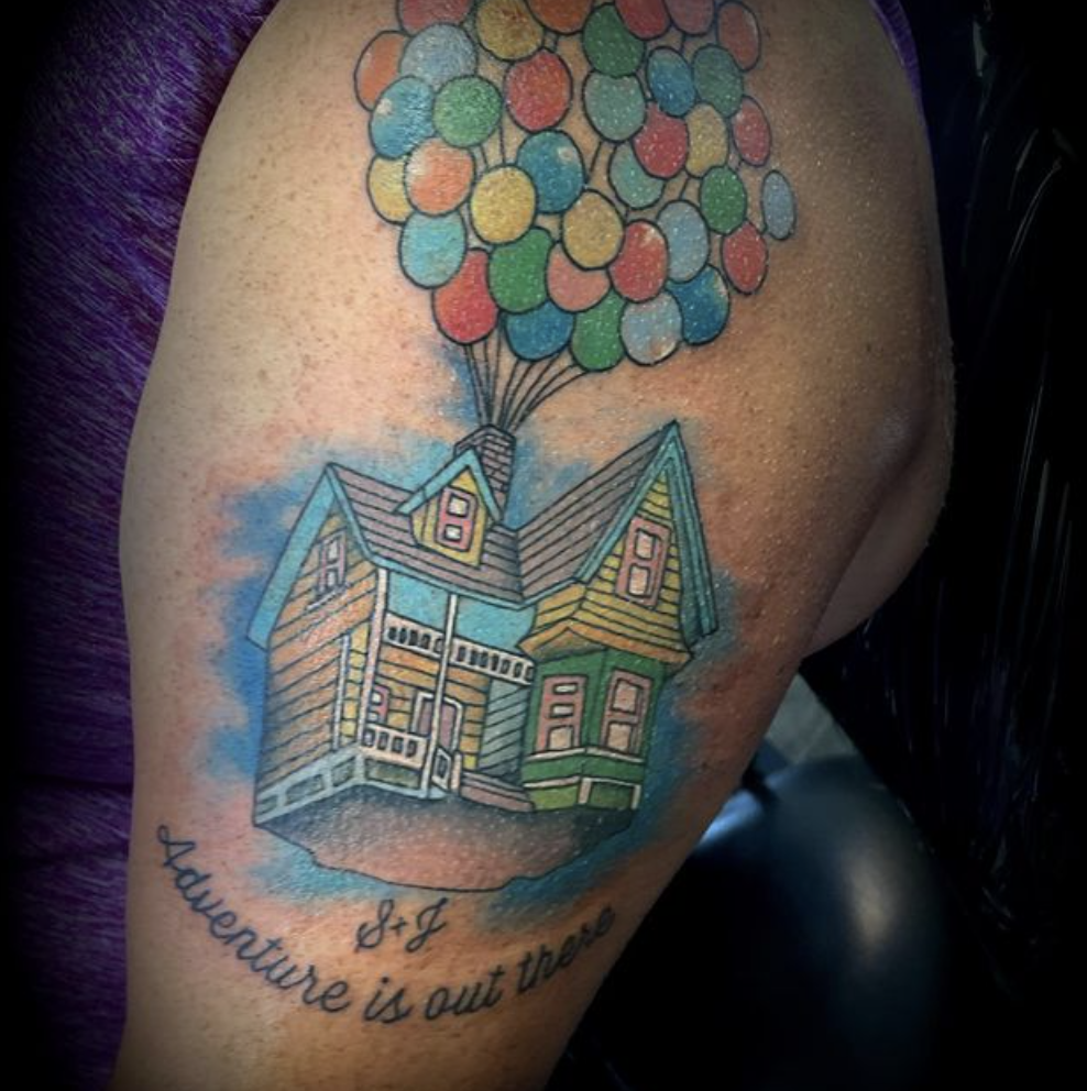 A tattoo of a house with balloons and the words adventure is out there