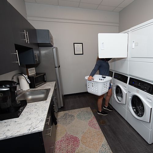 A woman is carrying a laundry basket in a laundry room.