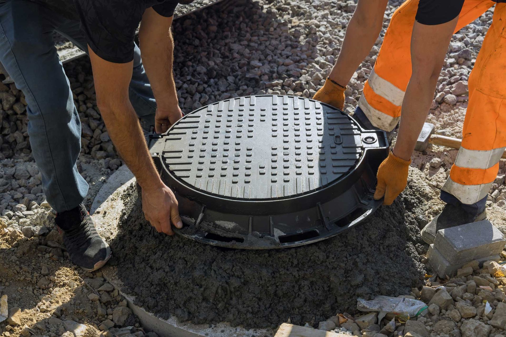 Two men are working on a manhole cover in the dirt.