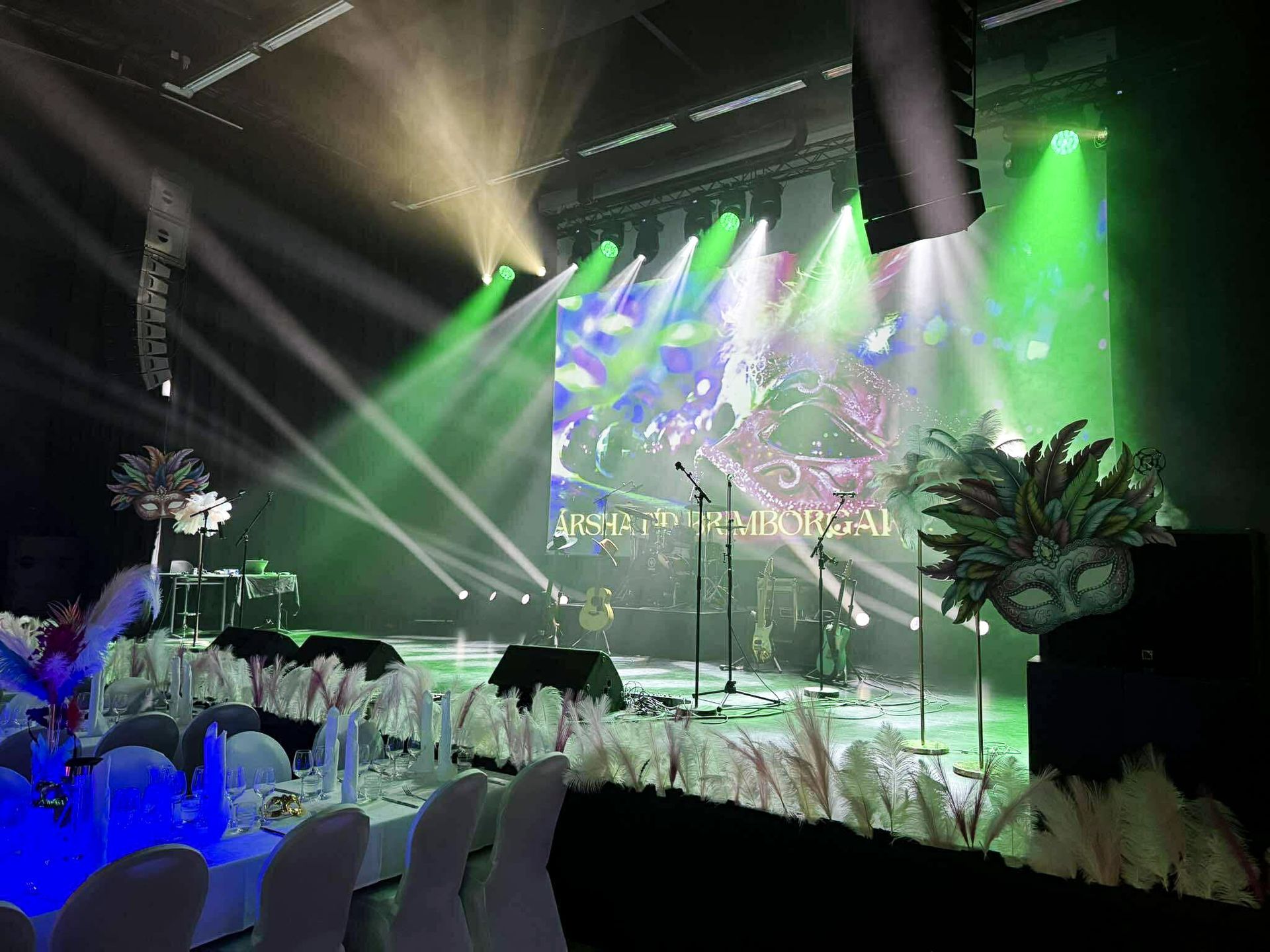 Decorated stage at Hljómahöll with feather centerpieces, colorful lighting, and a carnival-themed visual backdrop.