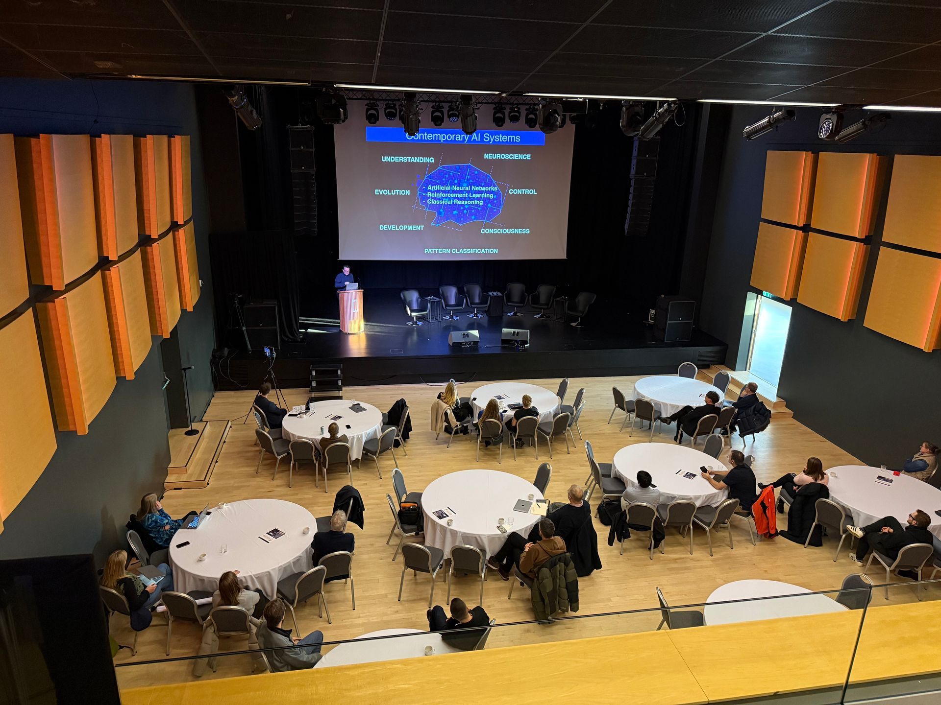 Speaker presenting on AI systems during a tech seminar at Stapi conference center.