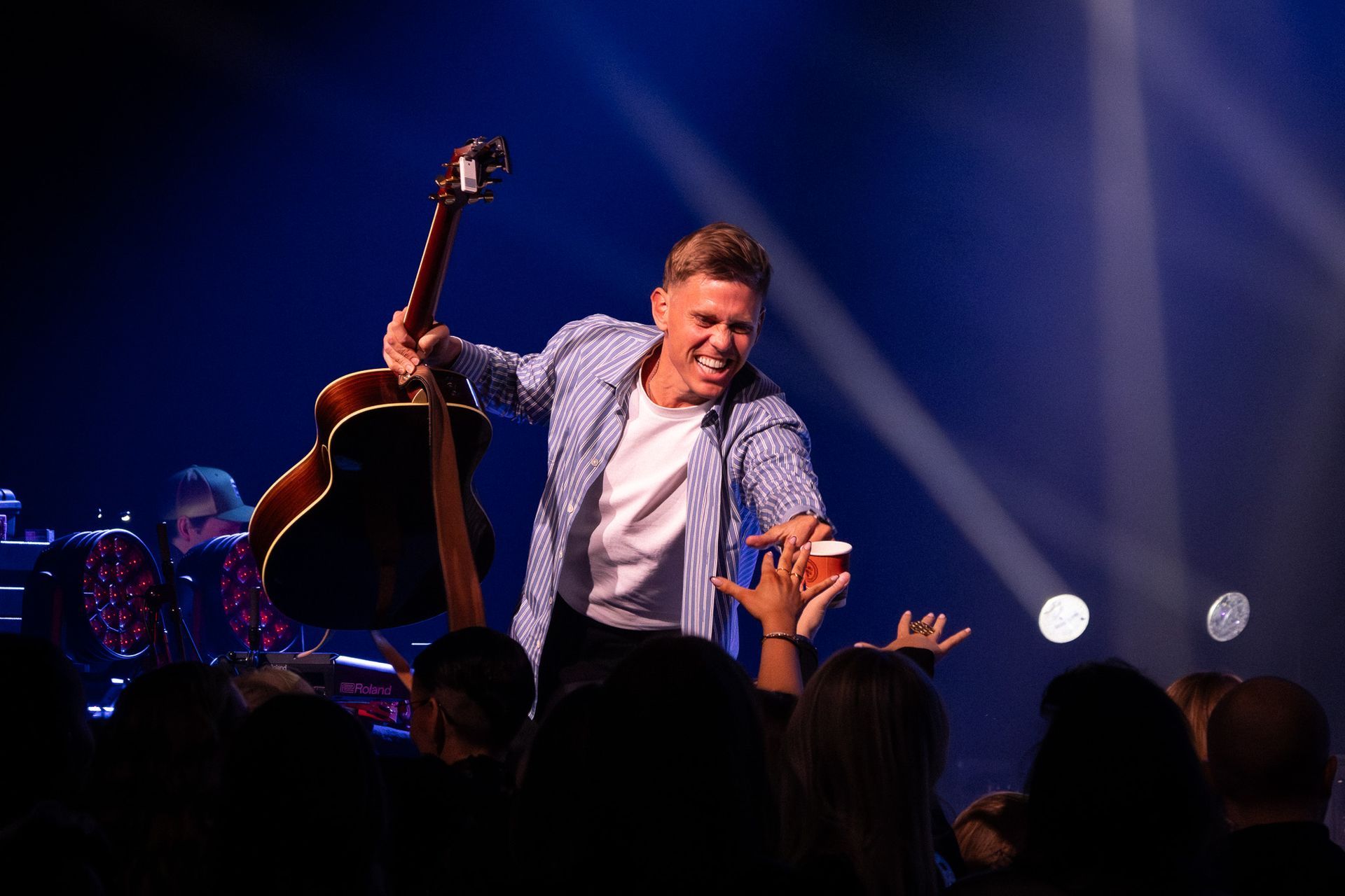 Jón Jónsson smiling on stage at Stapi, reaching toward fans while holding a guitar.