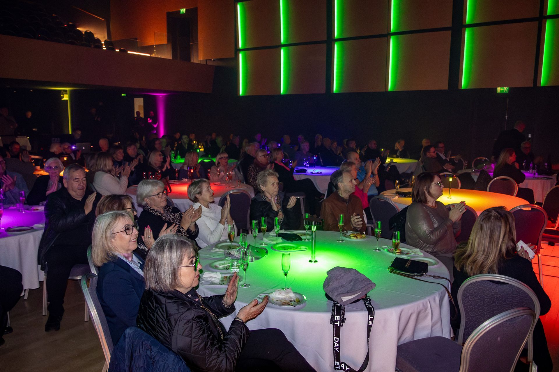 Audience enjoying a formal event at Stapi, seated around color-lit round tables.