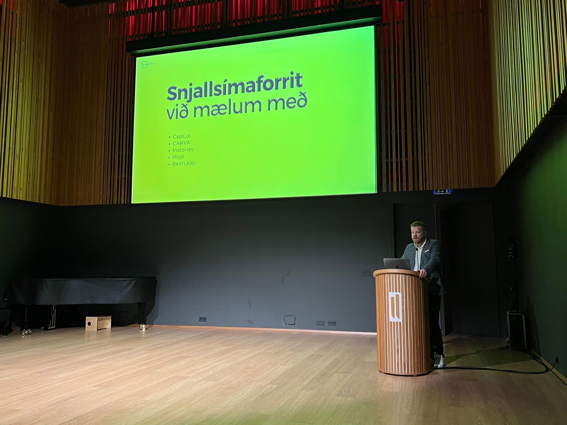 A presenter at a podium discusses recommended mobile apps, projected on a bright green screen.