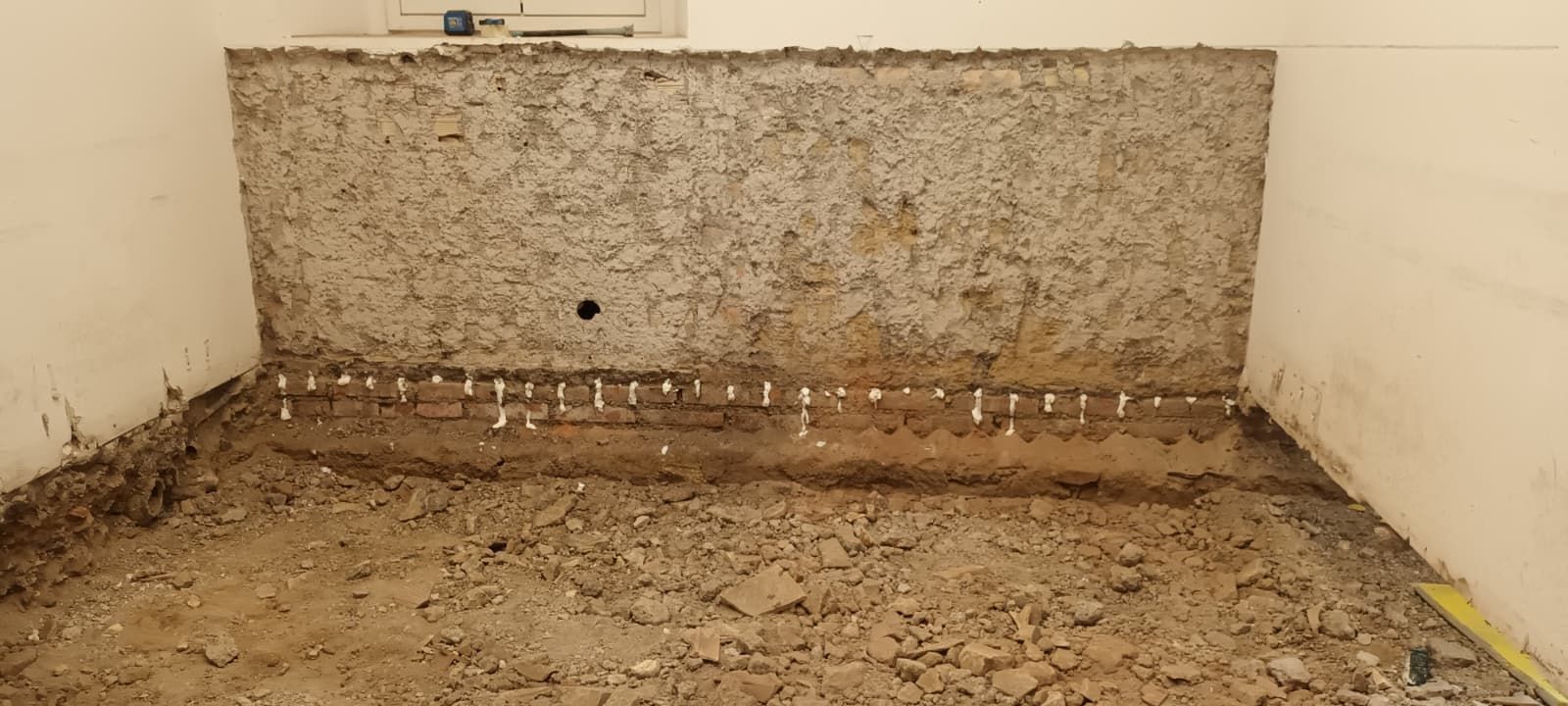 Interno sporco con muro di cemento a vista, una fila di pioli bianchi e pareti bianche.