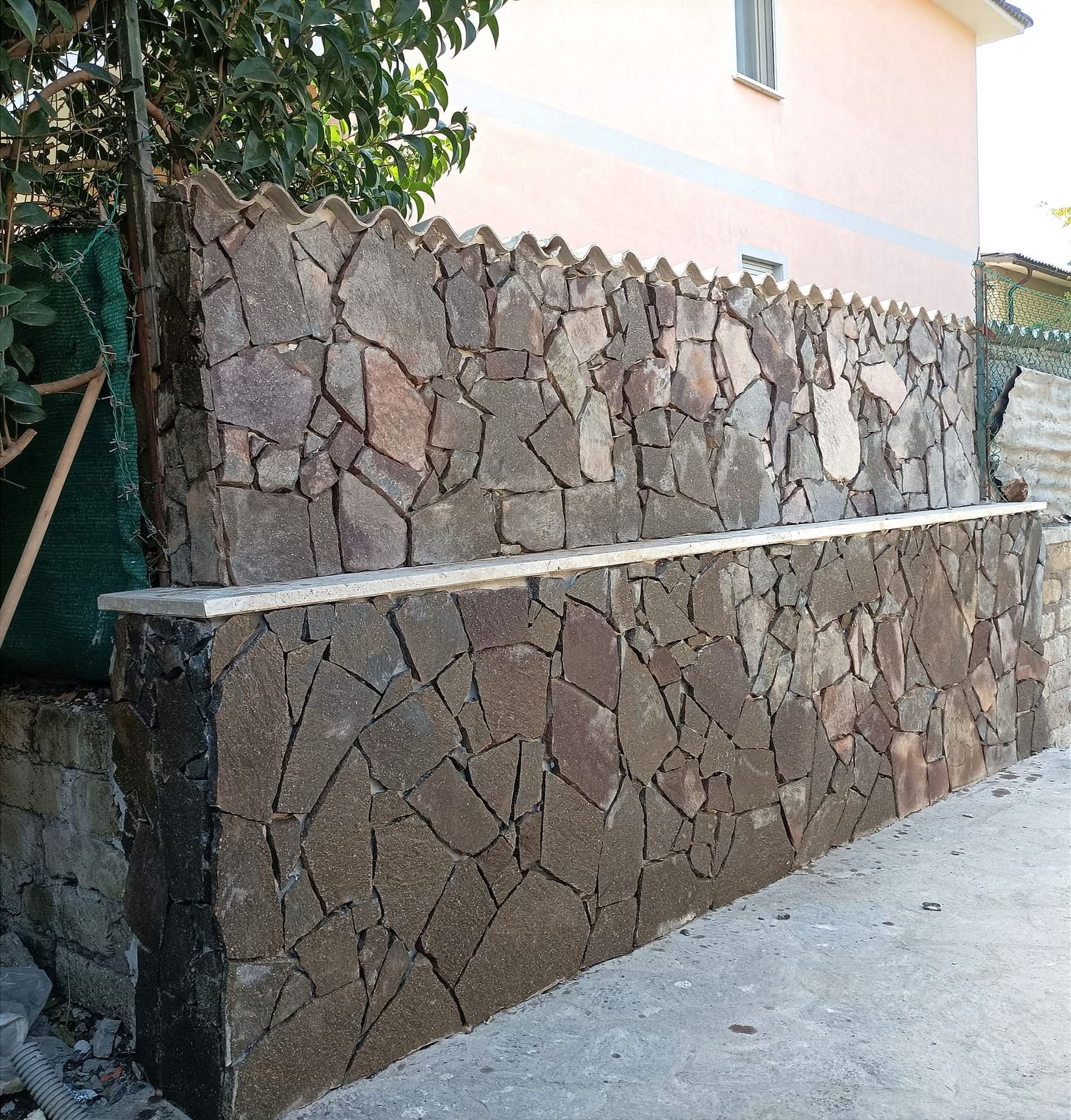 Muro di pietra con sommità frastagliata, pietre marroni e bordo in cemento.