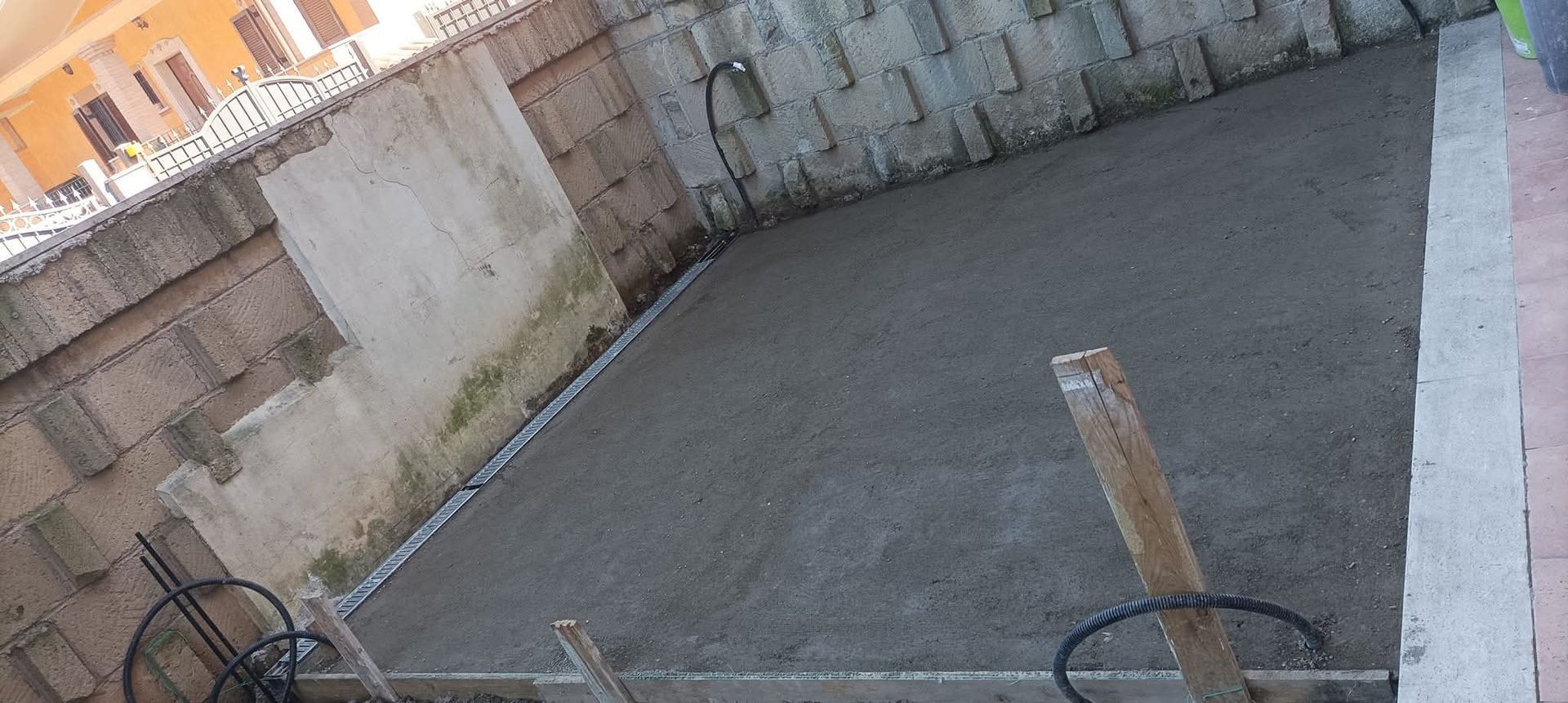 Una soletta di cemento viene gettata, delimitata da mattoni e da un marciapiede pavimentato, con supporti in legno.