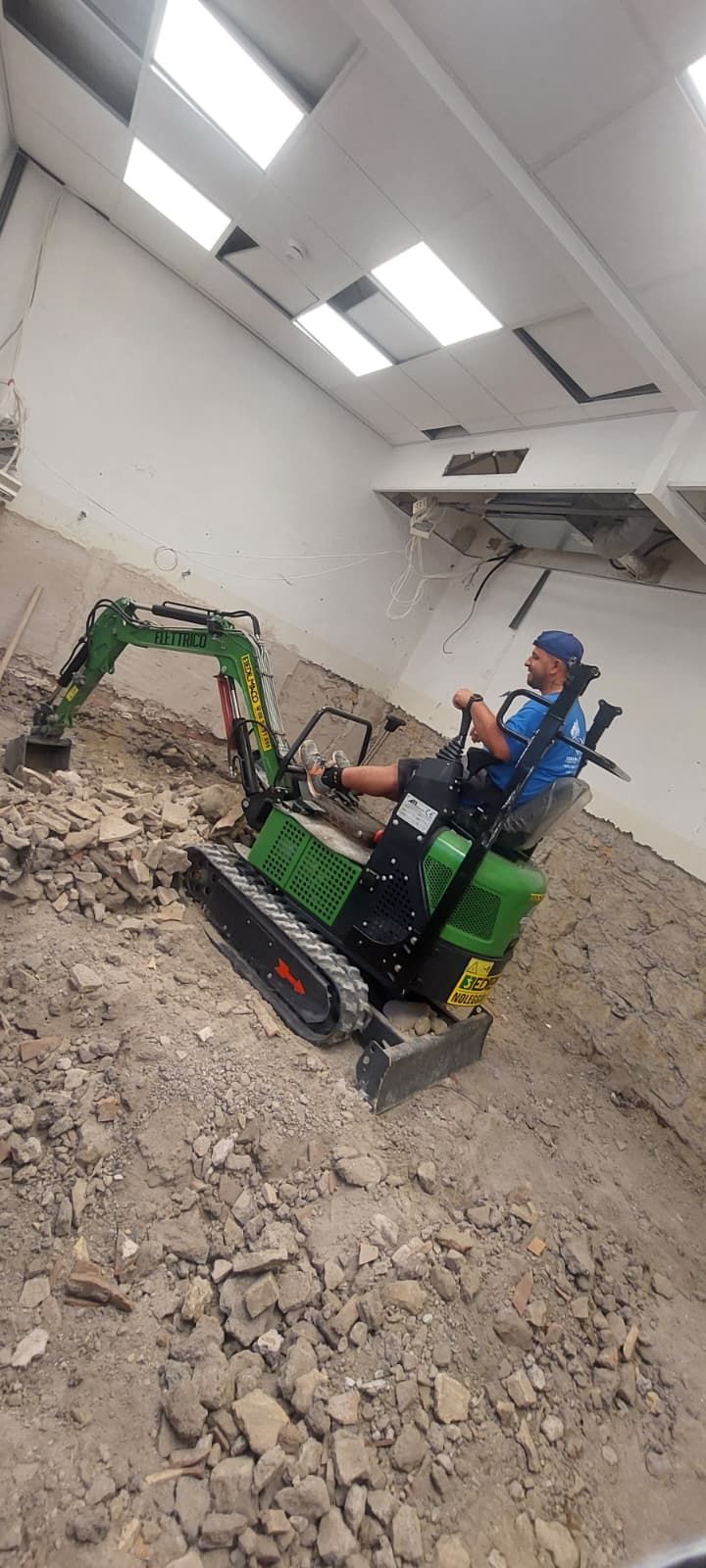 Una persona che aziona un miniescavatore ecologico all'interno di un edificio, probabilmente durante lavori di demolizione o costruzione.
