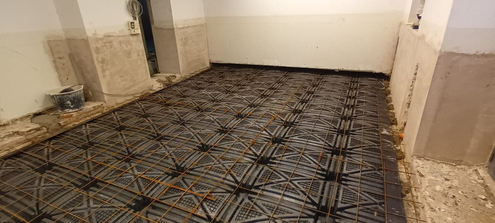 Rete di rinforzo in acciaio stesa su un pavimento in cemento, pronta per essere colata.