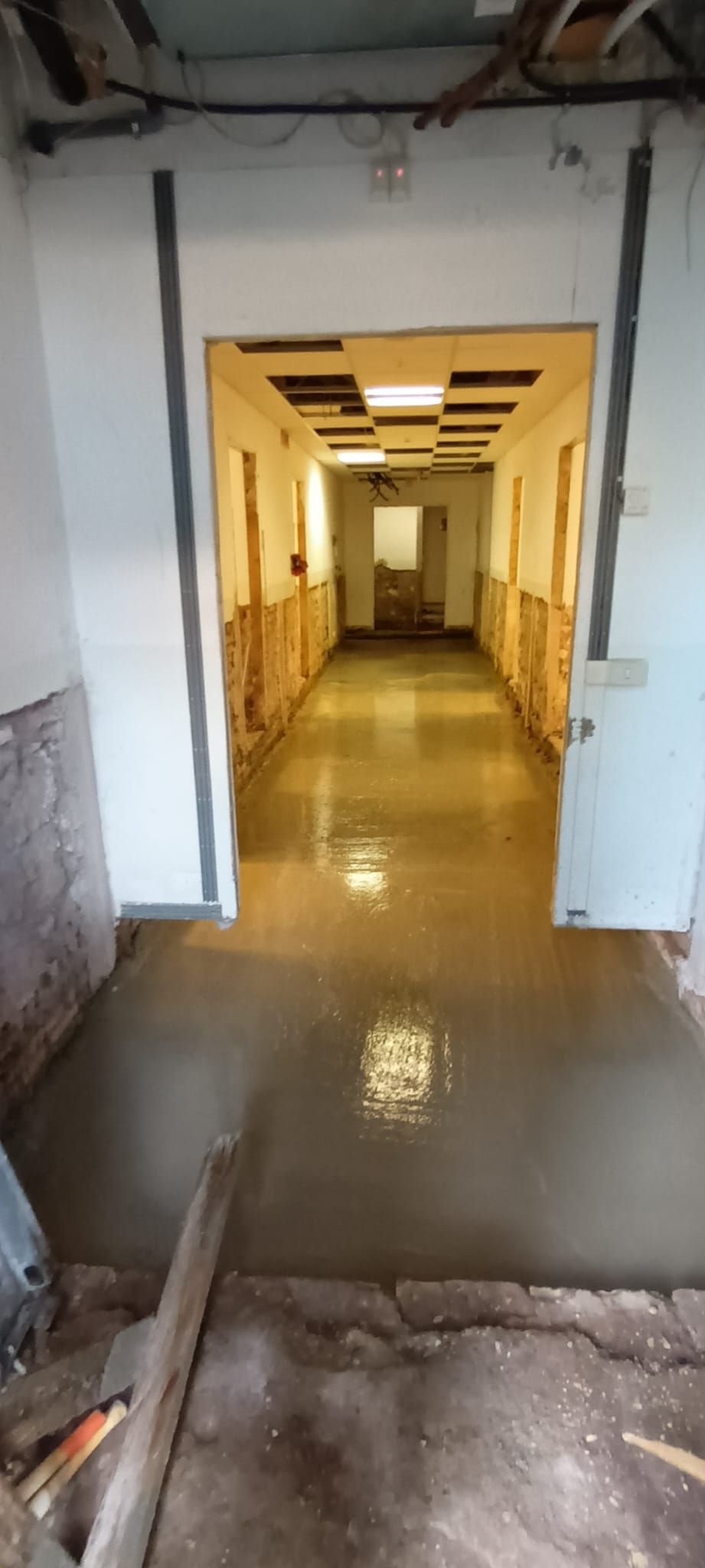 Un lungo corridoio con pavimento in cemento bagnato e soffitto aperto.