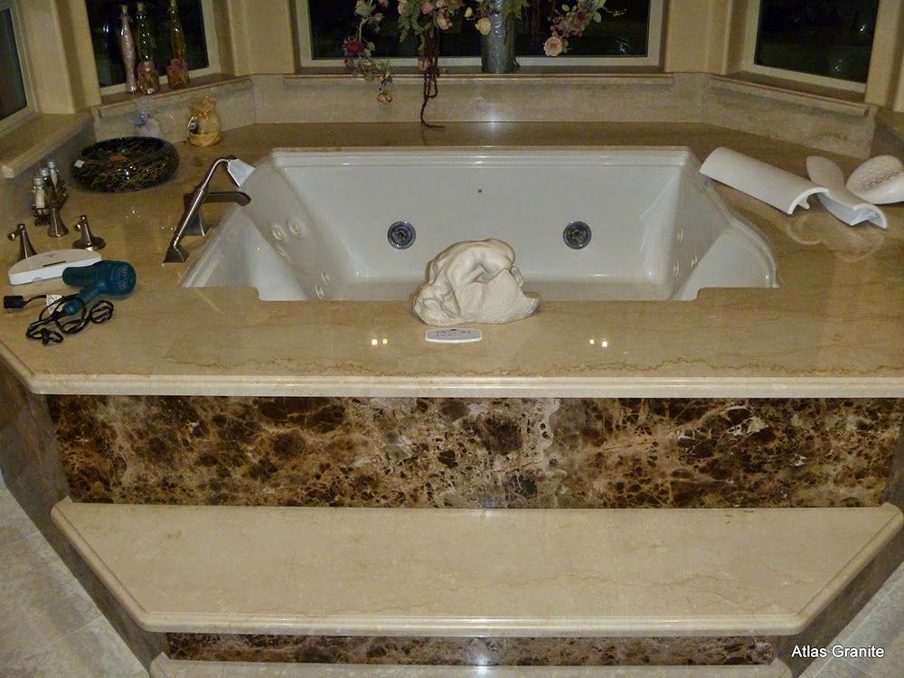 A luxurious beige and brown marble bathtub surrounded by a matching countertop and accents, with a window in the background.