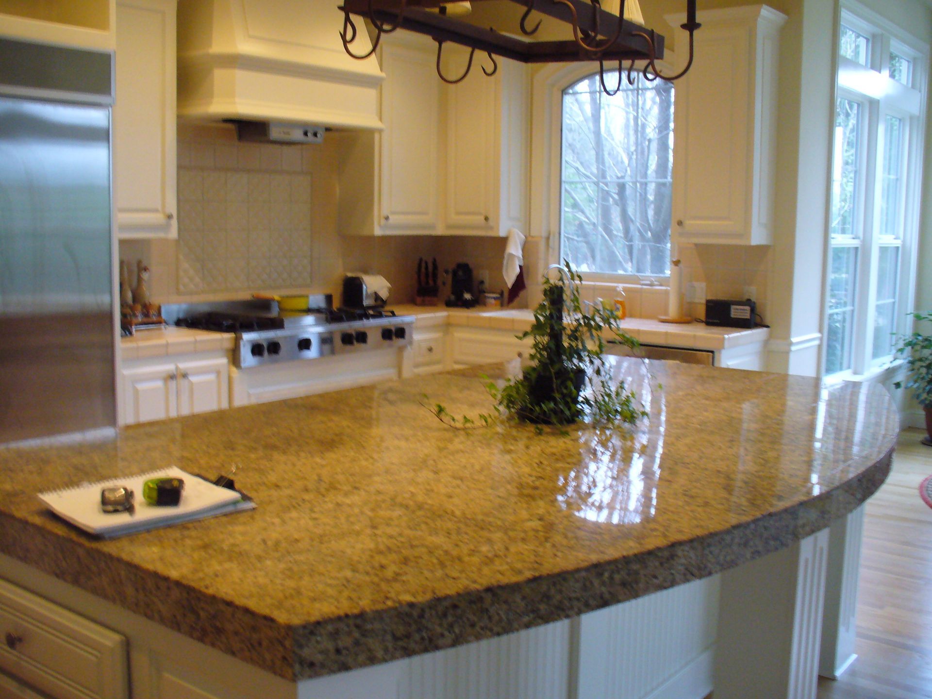 Kitchen with light-colored cabinets, a large granite countertop island, and a stainless steel refrigerator.