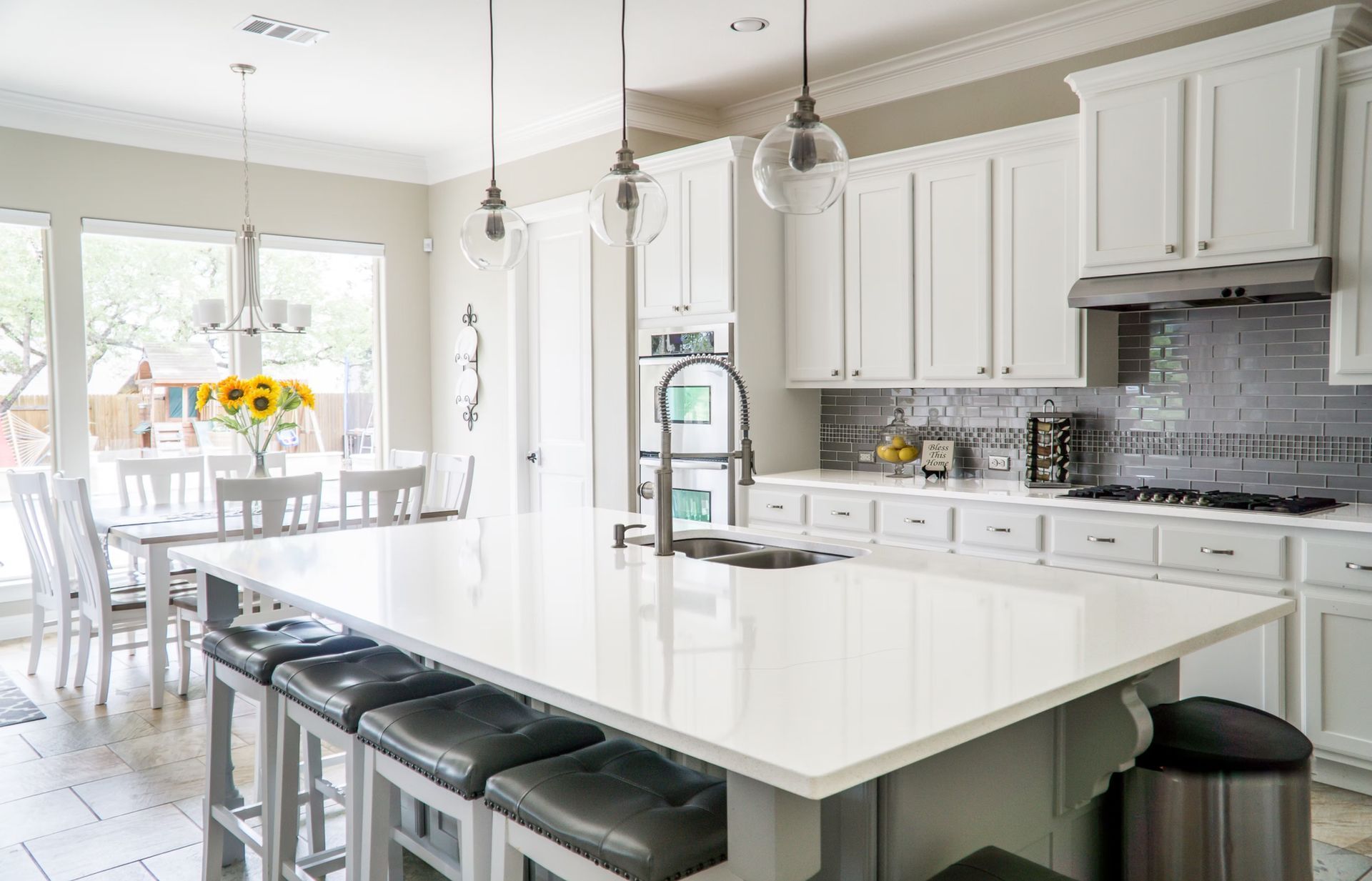 White kitchen with island and seating, white cabinets, and dining area with sunlight.