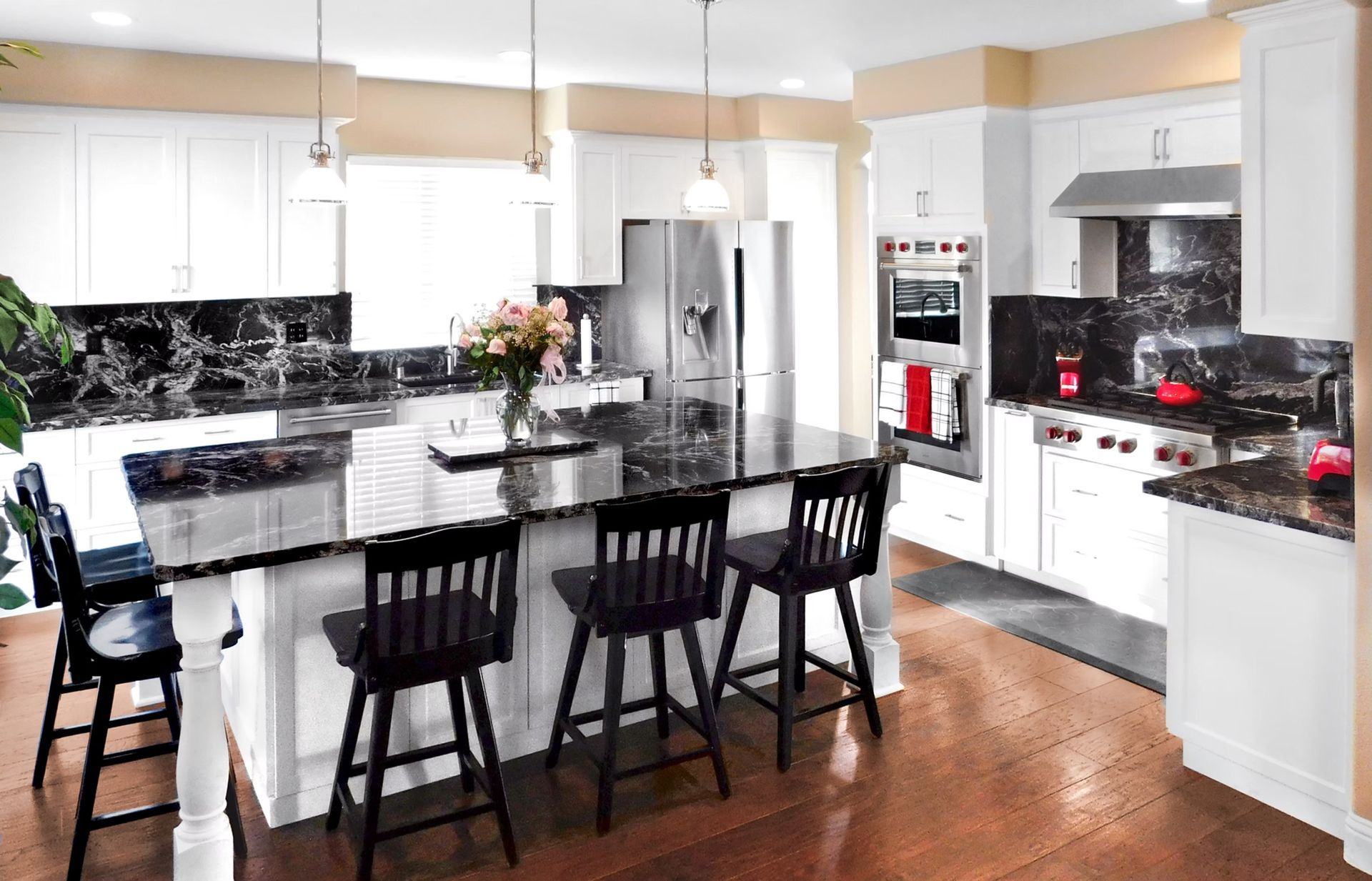 Modern kitchen with white cabinets, dark countertops, a large island with black stools, and stainless steel appliances.