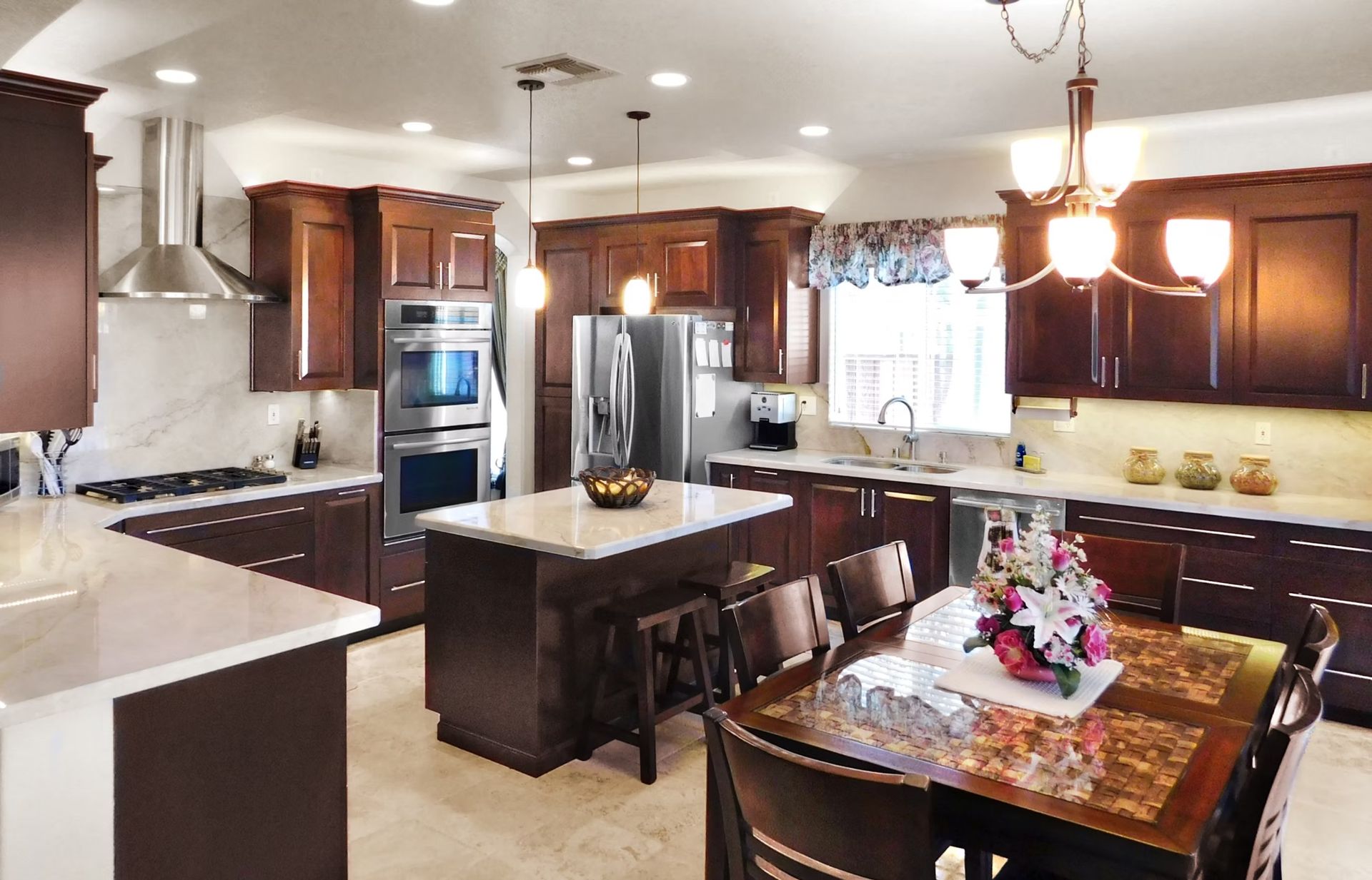 Spacious kitchen with dark wood cabinets, stainless steel appliances, and a marble countertop island and table.