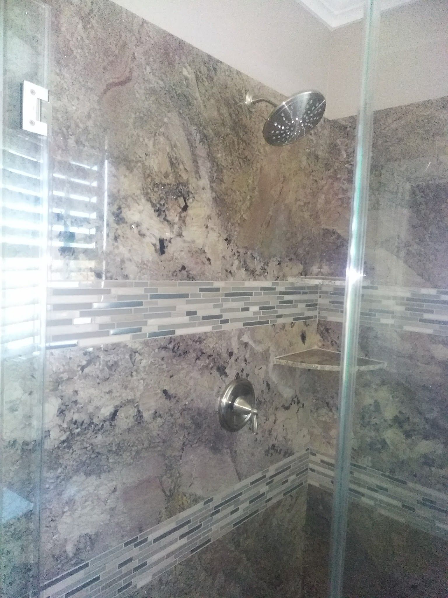 Shower with glass doors and granite tile walls, featuring a mosaic tile border and chrome fixtures.