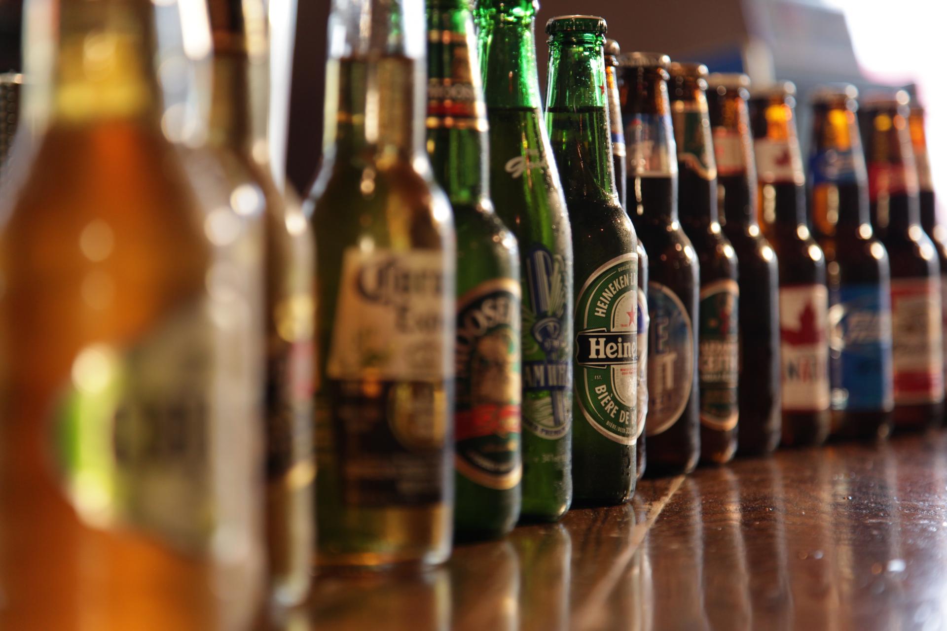 A row of beer bottles are lined up on a bar.