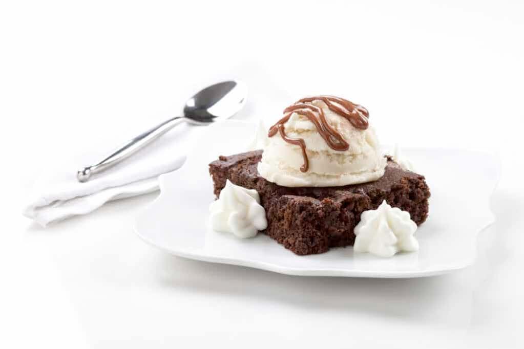 A brownie with ice cream and whipped cream on a white plate.