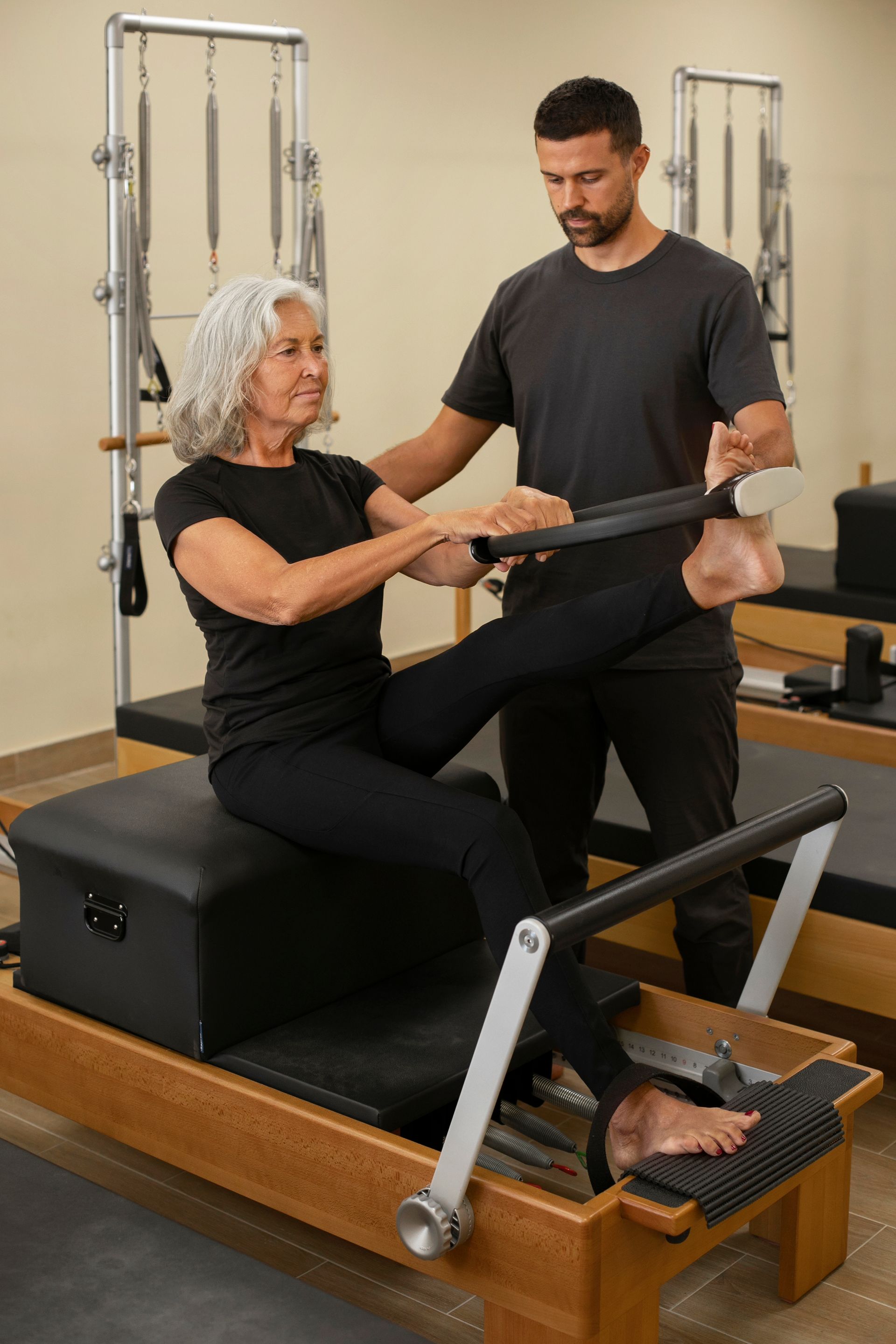 A man is helping an older woman do pilates on a pilates machine.