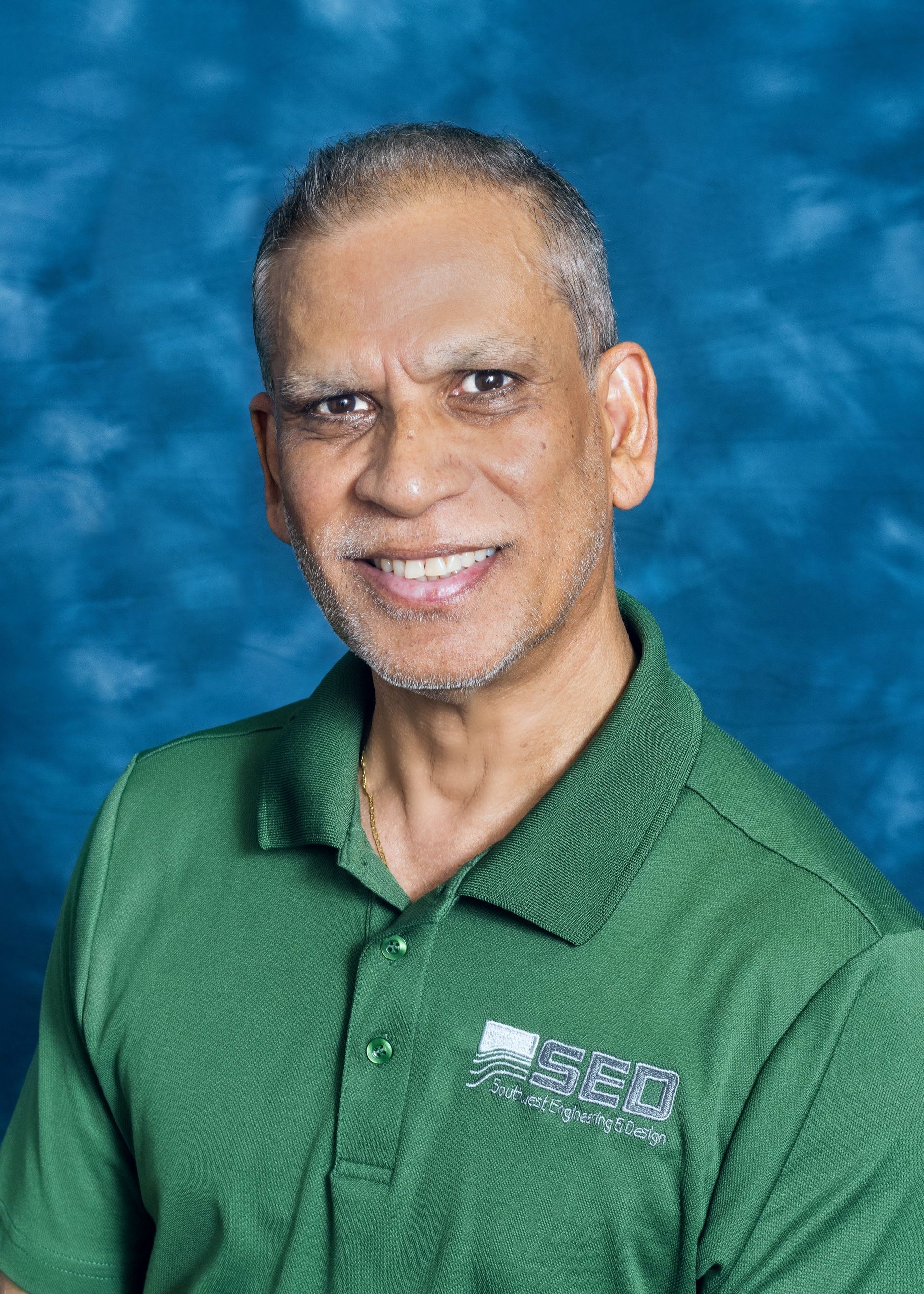 Smiling man wearing a green polo shirt against a blue textured background.
