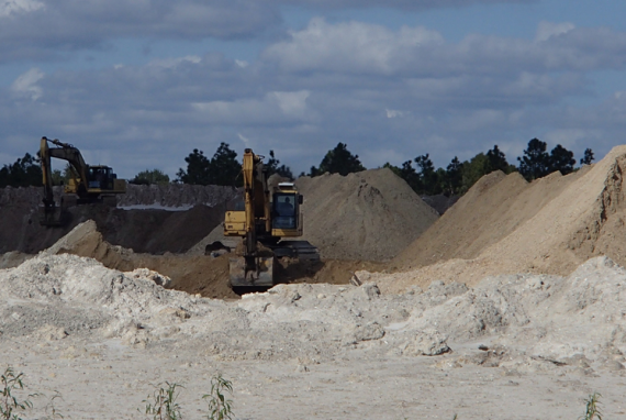 Two excavators digging in a sand and soil quarry under a cloudy sky.