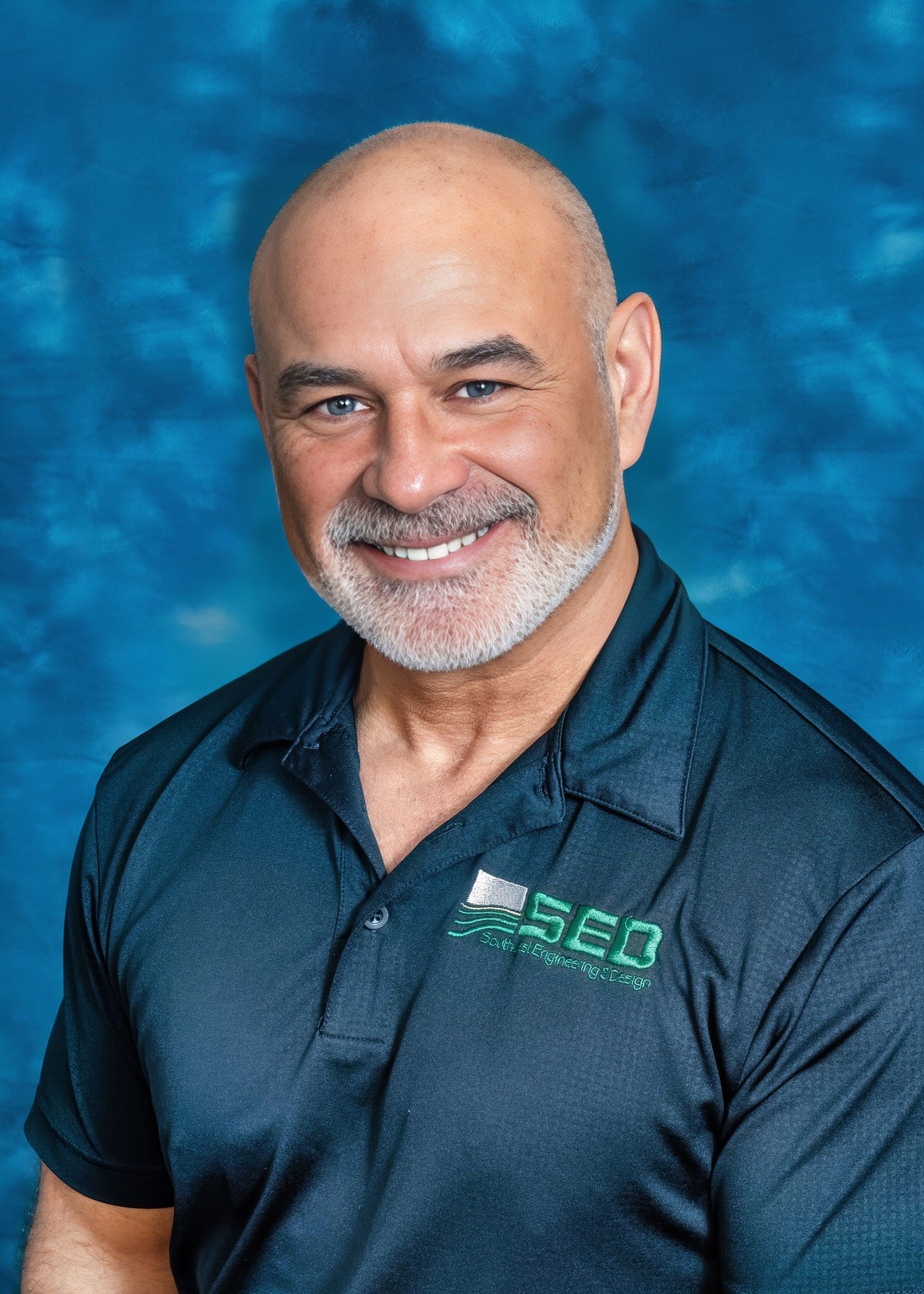 Bald man in a blue shirt smiling, with a backdrop of blue.