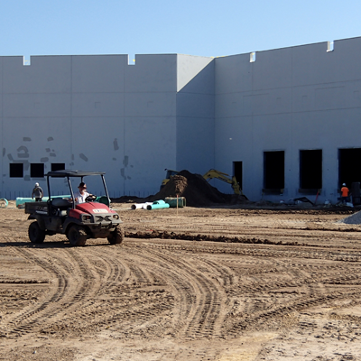 Construction site with workers and an ATV in front of a large gray building.