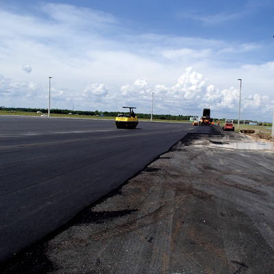 A yellow road roller compacting fresh black asphalt on a construction site.