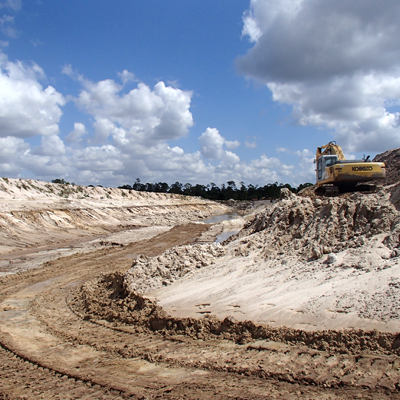 Excavator on a sand pit under a cloudy blue sky.