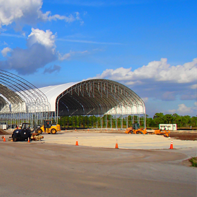 Large white arched-roof structures under construction, with construction vehicles and a blue sky background.