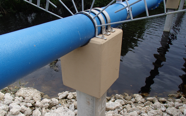Blue pipe supported by tan concrete over water.